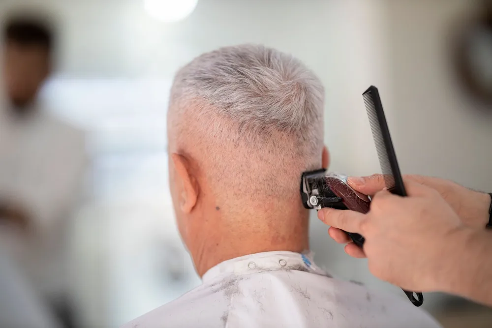Barbier réalisant une coupe à la tondeuse dans son salon