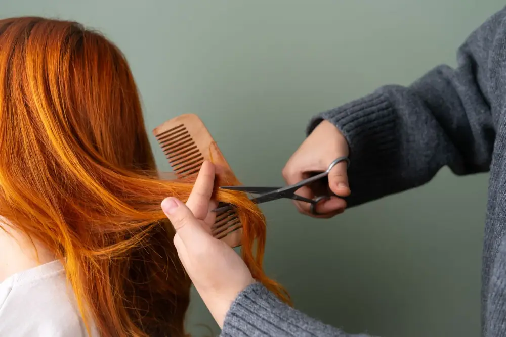 Coiffeuse coupant une mèche de cheveux roux aux ciseaux et au peigne