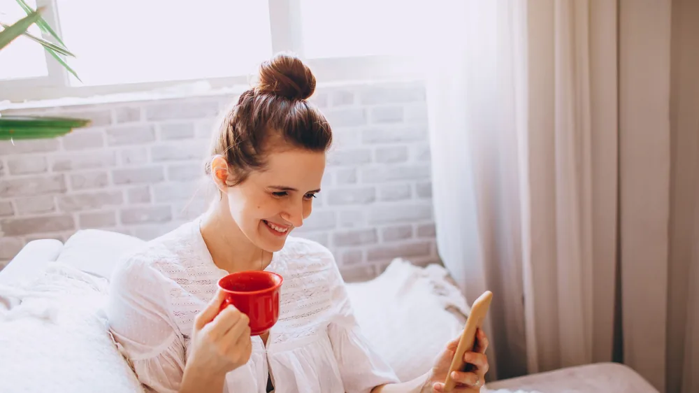 Femme lisant sur son smartphone, installée dans un canapé