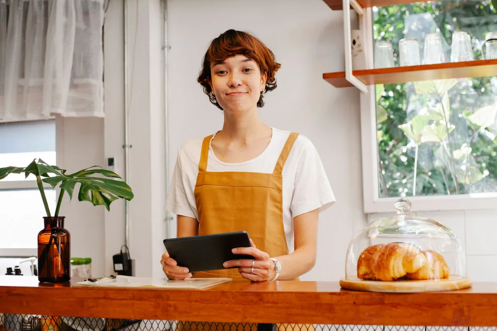 Gérante de café souriante tenant une tablette derrière son comptoir
