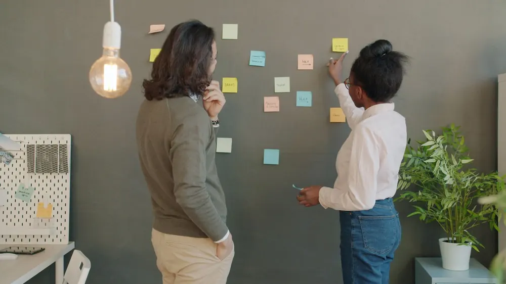 Deux personnes organisant un projet avec des post-it collés au mur