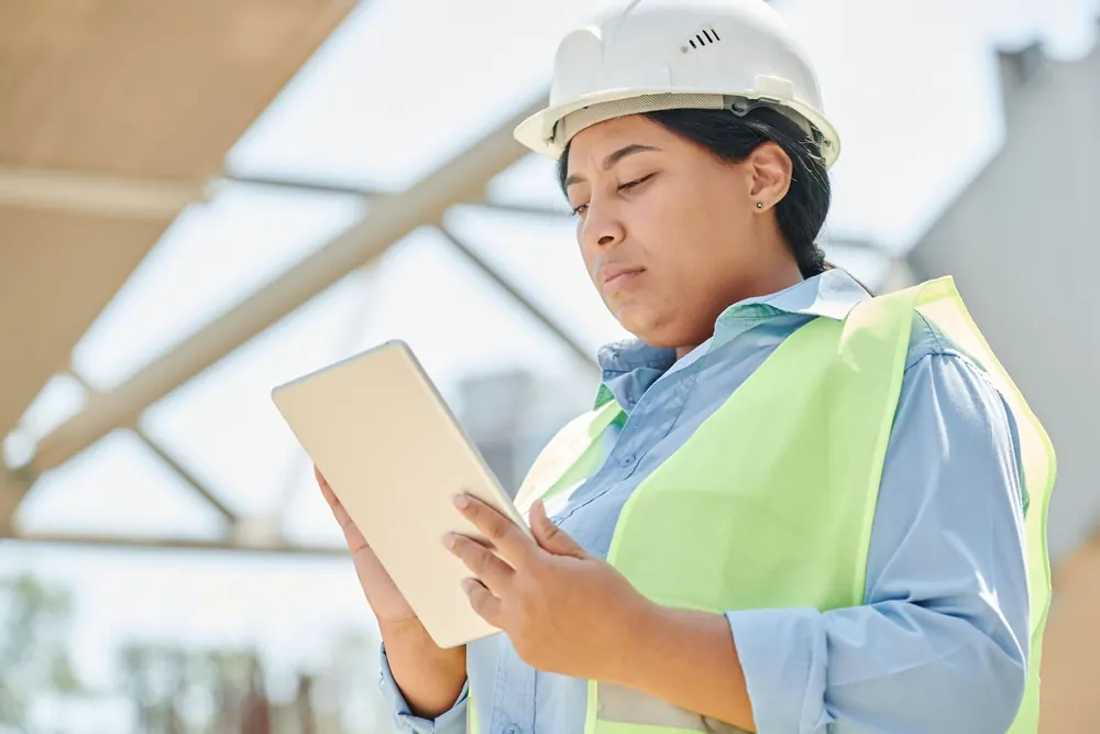 Cheffe de chantier en casque et gilet consultant une tablette sur le terrain