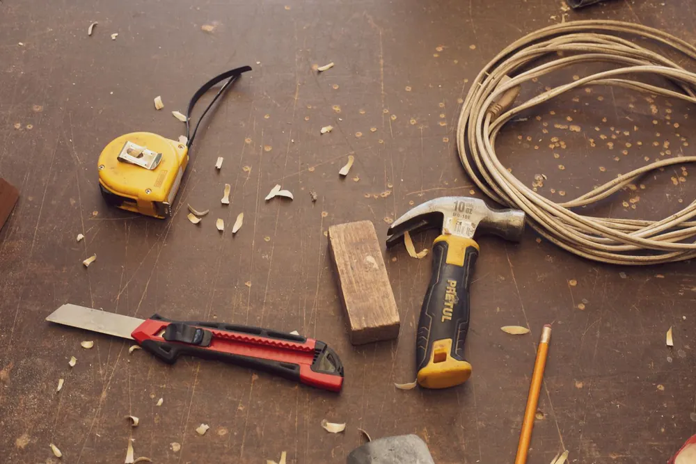 Outils de menuisier posés sur un établi : mètre, marteau, cutter et cordeau